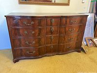 Front view of the wooden dresser showing twelve drawers, curved front, brass handles, and dark wood finish.