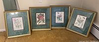 Photo shows all four framed floral prints arranged in a row on the floor, illustrating the full set and frame style.