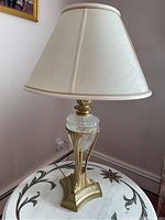 Full view of metal and glass lamp on a decorative table with cream colored shade