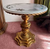 Side view of marble side table showing ornate gold painted carved wooden pedestal base and trim under marble top.