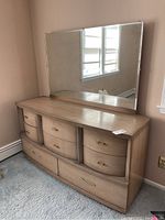 Wooden mid-century modern dresser with attached mirror seen front angle showing curved drawer fronts and gold-tone handles. Dresser surface shows scratches.