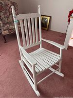 White wooden rocking chair with vertical slats on backrest and horizontal slats seat, showing wear including cracks and staining.