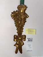 Close-up photo of one golden enameled ceramic wheat flower candle sconce with decorative bow, showing design details and ceramic texture.
