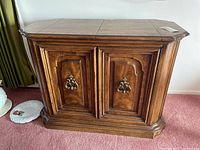 Front view of wooden sideboard cabinet showing two paneled doors with brass hardware and polished wooden finish.