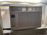 Front view of TCL 6W3ER1 window air conditioner installed in window with digital display showing temperature and control buttons.