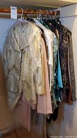Photo showing a variety of women's clothing hung on a rod, including a light colored blazer with a subtle pattern and some covered with plastic.