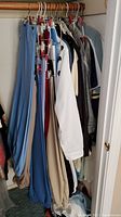 Closet rod with women's clothing items including slacks, blouses, jackets, blazers, coordinate sets hung on hangers.