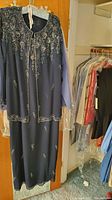 Dark blue dress and jacket set with silver embroidery displayed hanging on door