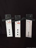 Front view of three wooden snowman boards with painted faces and hats against black background