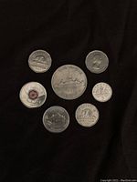 Seven coins arranged on black fabric background showing Canadian one cent coin 1961, Canadian 5 cents coin, British coins with monarch profiles, and other international coins.