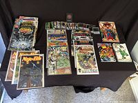 Full top-down view of all comic books and trading cards laid out on a black cloth, showing varied comic series and card packs.