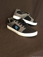 Pair of black and gray DC Shoes sneakers in men's size 9.5 shown from side angle on dark background.