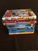 Stack of 10 Disney Blu-Ray and DVD cases including Cloudy with a Chance of Meatballs, Cars, Olive the Other Reindeer DVDs and Inside Out, Frozen, Rise of the Guardians, Brave, Wall-E, Lorax Blu-Rays.