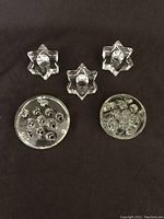 Top view of three star-shaped clear glass candle holders and two round candle holders with multiple indentations for candles.