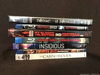 Seven horror movie cases arranged vertically showing titles: Zodiac, The Butterfly Effect, My Bloody Valentine 3D, Chernobyl Diaries, Insidious, Zombieland, The Cabin in the Woods.
