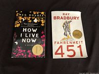 Top view of front covers of both paperback books 'How I Live Now' and 'Fahrenheit 451' placed side by side on a black background.