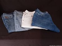 Four pairs of men's jeans shown folded on black background in different shades of denim including one white pair