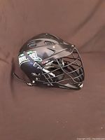 Left side view showing black helmet, Whalers decal and metal cage face mask