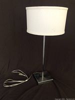 Front view of the lamp showing the white fabric shade and metal base with visible cord and plug.