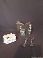 Photo showing all items including stone coasters with airplane cutouts, metal handles, glass candle holder wrapped with twine, and black wooden block with 'HOME' text.