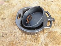 Two stacked black plastic oil catcher pans shown on dry grass; larger rectangular pan underneath, smaller round pan with attached hose on top