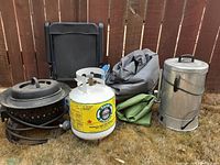 Photo showing entire lot of outdoor camping supplies: firepit, propane tank, tarps, chair, metal smoker.