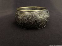 Front view of the wide silver bangle showing detailed hand engraving of foliage and birds pattern.