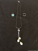 Full set of items: silver necklace with pearl pendant and two silver rings on black background