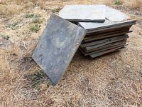 Side view of stack of square grey concrete floor tiles placed on dry grass showing thickness and size
