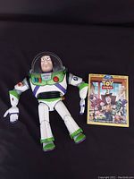 Buzz Lightyear action figure laid flat with Toy Story 3 DVD case beside it, showing front view.
