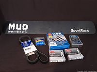 Various car parts including belt, spark plugs, blue rubber grommets, blue connectors, and fuse kit arranged on black background