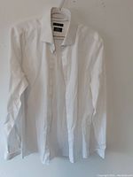 White long sleeve dress shirt hanging on white plastic hanger against plain background.