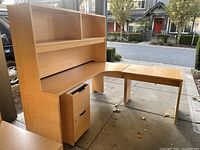 Overall view of the light wood L-shaped desk with upper hutch and mobile pedestal on wheels. Shows condition and setup of the desk lot.