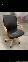 Front view of black leather office chair with wooden frame and caster wheels