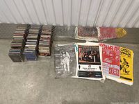 Photo showing multiple stacks of CD jewel cases and folded paper posters with band names and concert information.