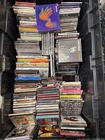 Top-down view of assembled rock and roll CD collection in a black storage bin showing many stacked jewel cases and cardboard slipcases.