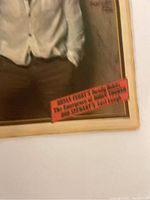 Partial photo of a framed image or poster with a white-shirted figure and a red label containing text about Brian Eno and text by Alex.