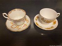 Two Royal Albert teacups with matching saucers, one pink floral Queen Anne pattern with gold trim, one yellow floral pattern on white.