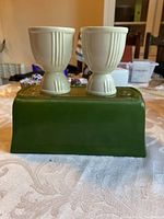 Front view of two ivory ceramic egg cups placed on top of a green rectangular glass planter base.
