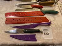 Overview of assorted knives and sharpening steel with colored knife guards and wooden handles on a table.