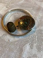 Photo showing vintage brass thimble, mother of pearl pillbox, and silver bracelet together on fabric surface.
