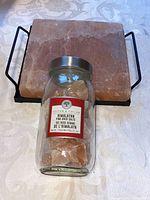 Square Himalayan salt cheese board on metal handles with jar of large pink salt rock chunks placed on top.