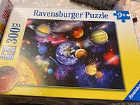 Closed box of Ravensburger 300 piece XXL puzzle featuring planets and space scene.