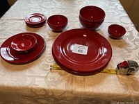 15 pieces of red Waechtersbach ceramic dishes in various sizes arranged on a table including large, medium, and small plates as well as bowls, showing the glossy ceramic finish and vibrant red color.