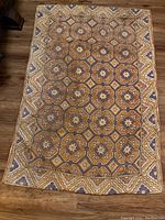 Full view of the prayer rug on a wooden floor showing overall pattern and condition.