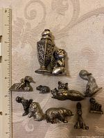 Top-down view of 10 small pewter or metal figurines including animals and an angel with a ruler for scale