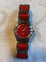 Front view showing red dial with stainless steel case and red inserts on bracelet links.