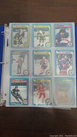 Photo of hockey cards in a binder showing nine cards in clear sleeves, players in various poses and teams with O Pee Chee design from 1979-80 season.