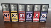 Front view of six mini stick boxes showing player names, numbers and team colors.