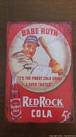 Photo of a rectangular vintage metal advertising sign for Red Rock Cola with Babe Ruth image and text.